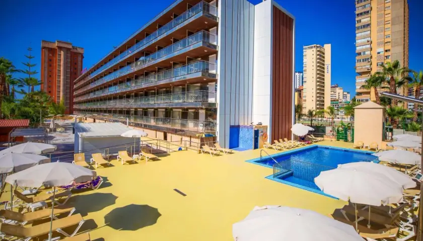 Terraza soleada con piscina y tumbonas en el hotel Diplomatic Benidorm. Edificio moderno con balcones y palmeras.