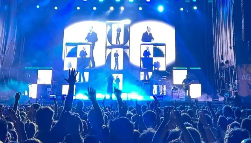 Multitud en concierto de Vetusta Morla en Valencia. Luces azules y pantallas con imágenes de los miembros de la banda crean un ambiente electrizante.