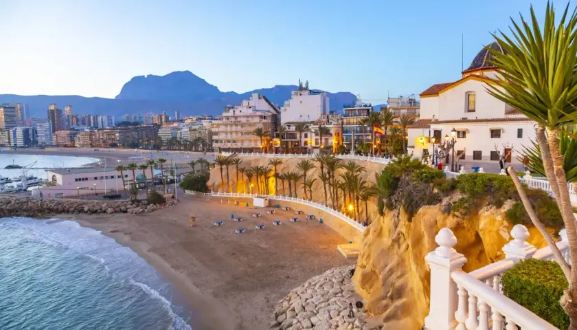 Atardecer en la playa Poniente de Benidorm, con el mar azul, la arena dorada, palmeras y edificios modernos.