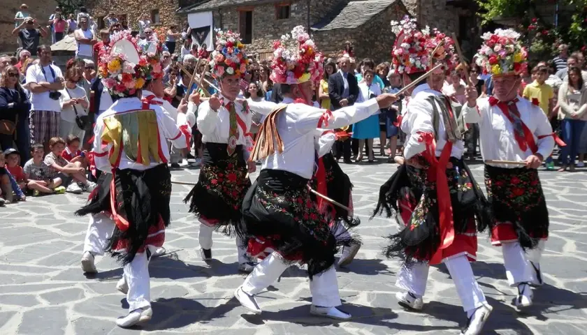 Hombres con trajes tradicionales y sombreros florales bailan en la plaza durante el **Día del Corpus**.
