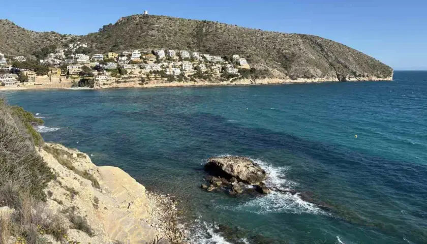Vista de calas y acantilados con casas blancas en la ladera, aguas turquesas y un peñasco en el mar. Playas bonitas cerca de Benidorm.