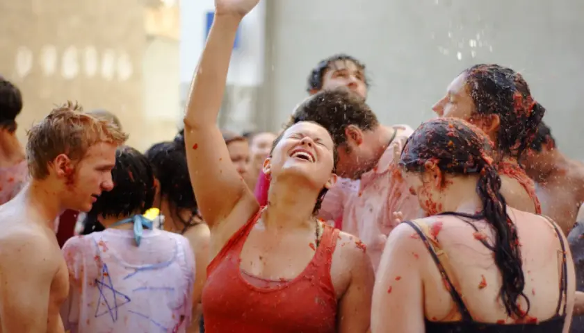 Gente feliz y empapada de tomate en la Tomatina, con una mujer riendo a carcajadas y el brazo en alto.