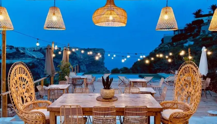 Un rincón de ensueño en el **dreamsea mediterranean camp**. Mesas de madera, sillas de ratán y luces cálidas bajo un cielo estrellado.