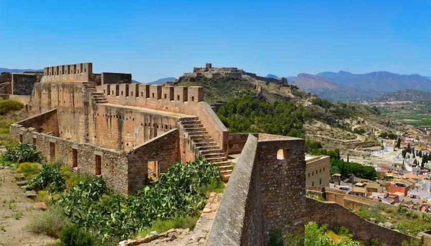 Ruinas del castillo de Sagunto, con sus imponentes murallas de piedra y escalinatas, dominan el paisaje montañoso.
