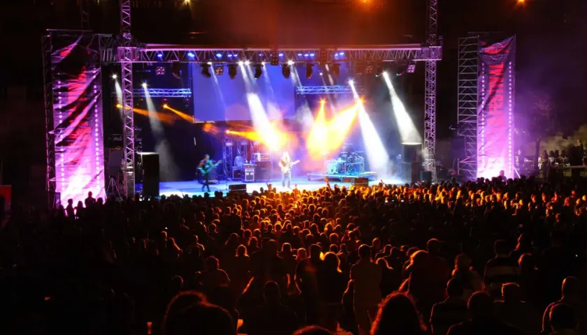 Multitud disfrutando de un concierto en un som festival, con luces brillantes y músicos en el escenario.