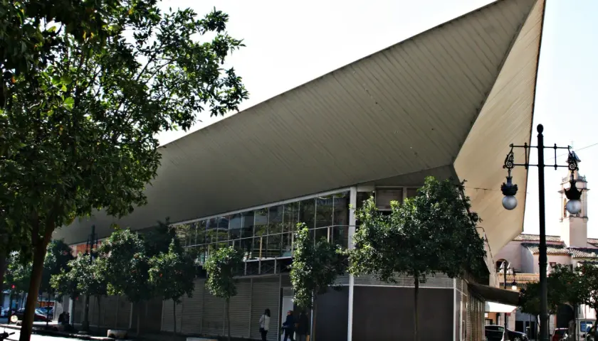 Edificio moderno con techo triangular y árboles en la calle frente al mercado de Jesús.