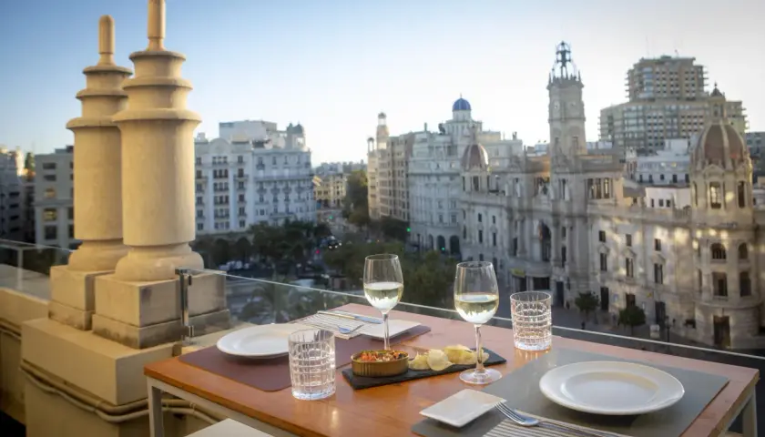 Una mesa en una terraza con vistas a la ciudad, con copas de vino y aperitivos, bajo el cielo de Atenea.