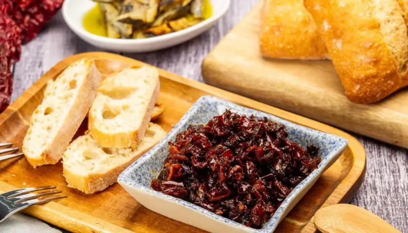 Pericana receta: pan rústico, pimientos secos y un cuenco con la deliciosa pericana, lista para untar.
