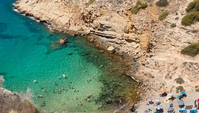 Aguas cristalinas y gente disfrutando en una cala rocosa, un paraíso que recuerda a las mejores calas de Benidorm.