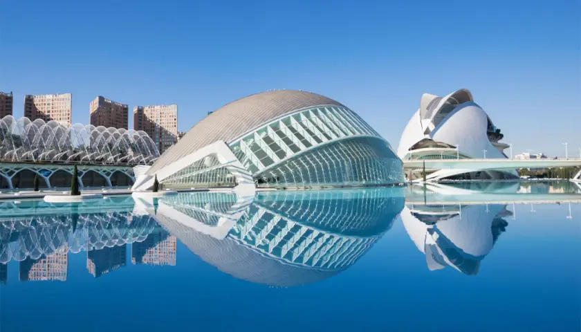 El Hemisfèric de Valencia, con su reflejo en el agua, se alza majestuoso bajo un cielo azul.