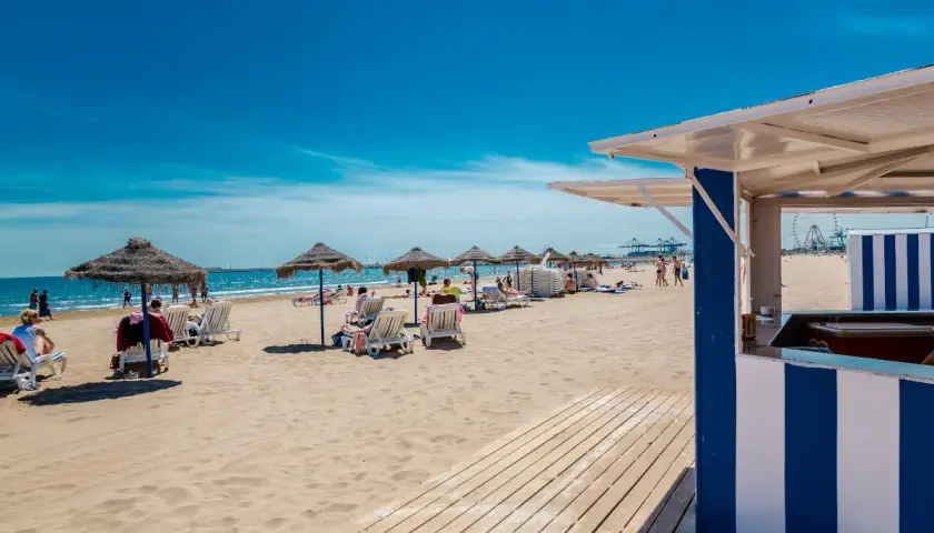 Día soleado en la strand Valencia. Sombrillas, tumbonas y gente disfrutando de la arena dorada y el mar azul.