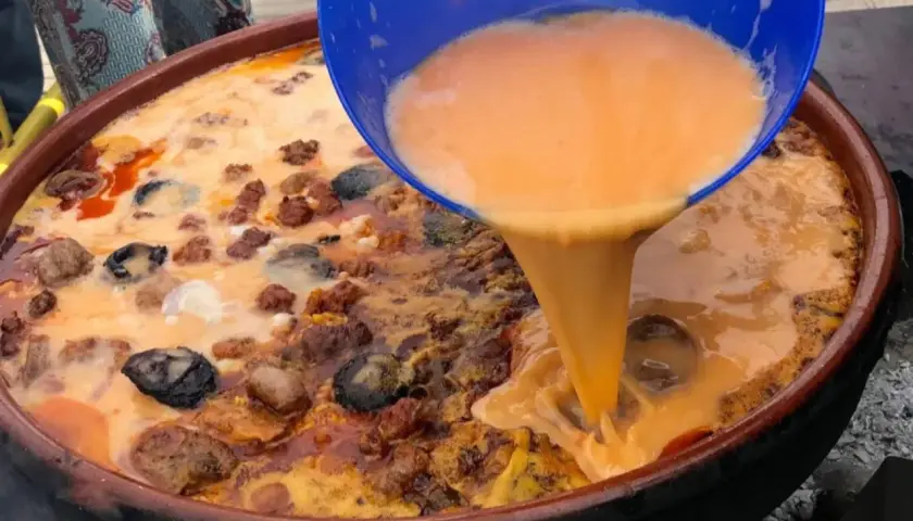 Un líquido naranja se vierte de un recipiente azul a una paella con carne y marisco.