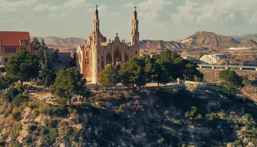 El **santuario** de Novelda se alza majestuoso sobre una colina, rodeado de vegetación y con un paisaje árido de fondo.