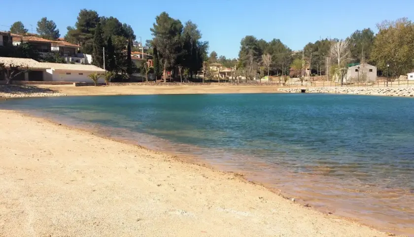 Arena dorada y aguas turquesas en la playa de Monte Navarrés, rodeada de pinos y casas.
