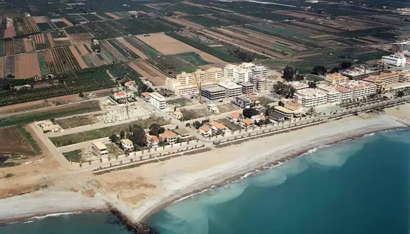 Vista aérea de la costa de Moncofa, con edificios residenciales y campos agrícolas. La playa de Moncofa se extiende hacia el mar turquesa.