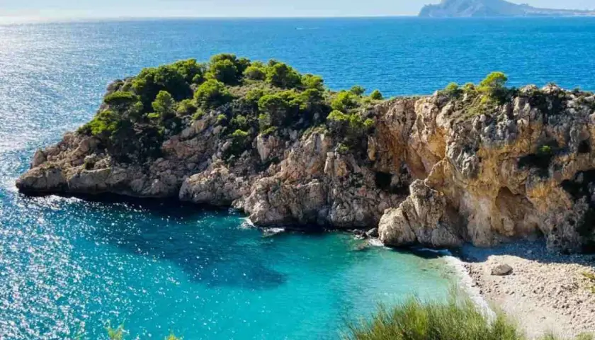 Una cala escondida con aguas turquesas y rocas escarpadas, un rincón idílico entre las mejores calas de Altea.