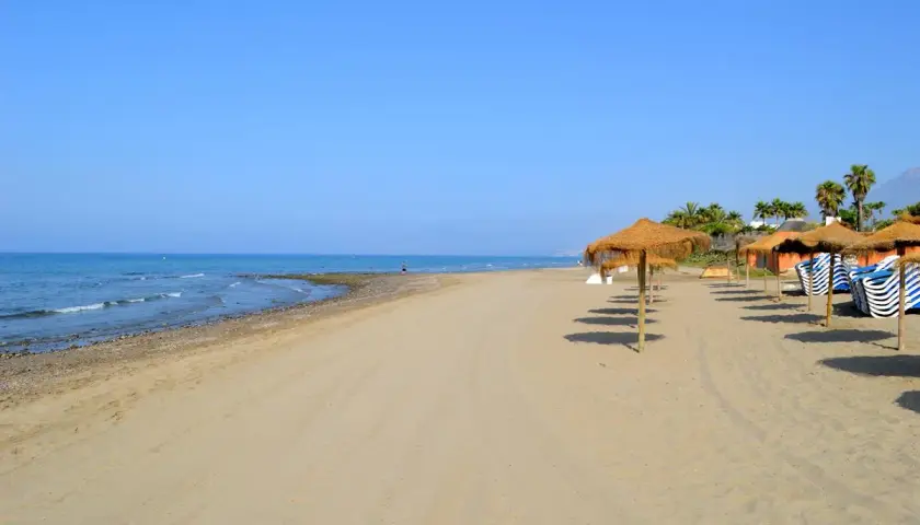 Arena dorada y mar azul en la playa de Alicante, con sombrillas de paja y tumbonas listas para disfrutar del sol.