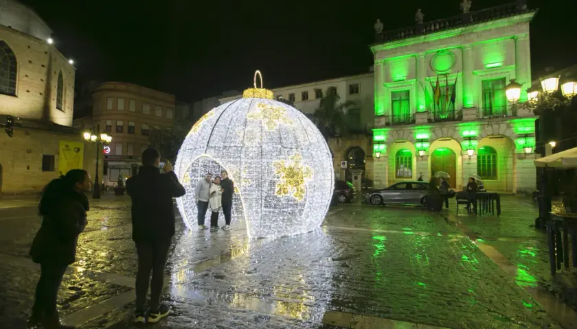 Una gran bola de luces ilumina la plaza en esta nit de cap d'any. Gente se hace fotos junto a la decoración.
