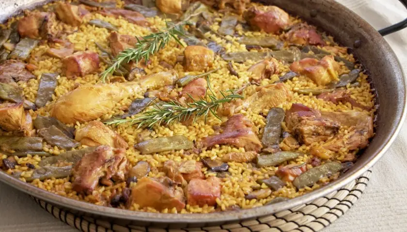 Paella valenciana recién hecha, con arroz amarillo, trozos de pollo, judías verdes y romero fresco.