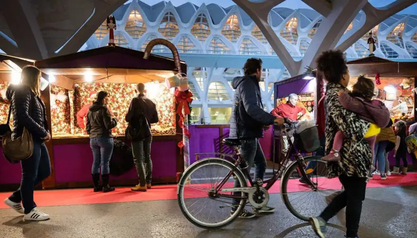 Gente pasea por puestos del **Valencia Christmas Market** bajo una estructura futurista.