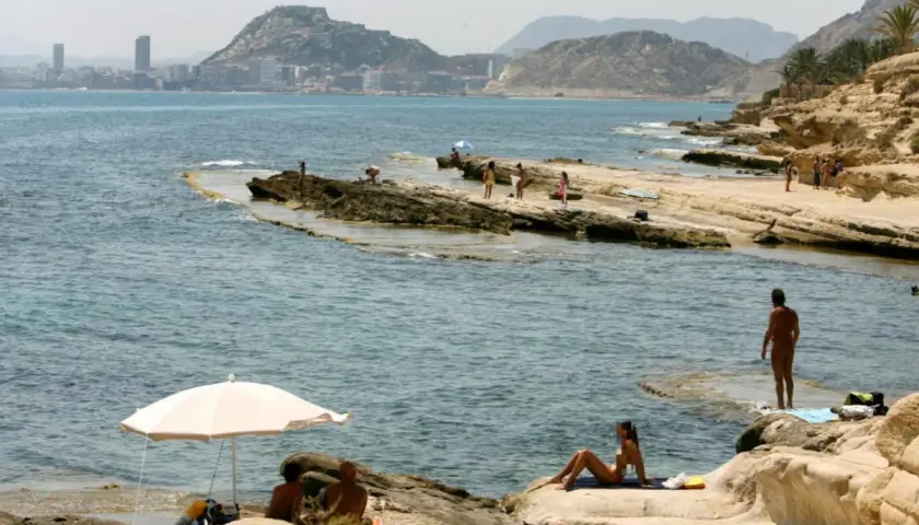 Gente disfrutando del sol y el mar en las playas nudistas de Calpe, con la ciudad al fondo.