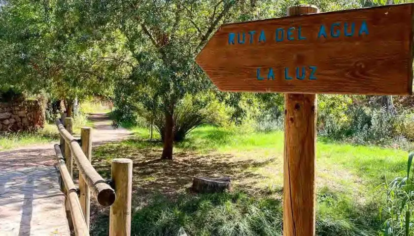 Cartel de madera indica "Ruta del Agua" y "La Luz" en Chelva. Camino de tierra con barandilla de madera.