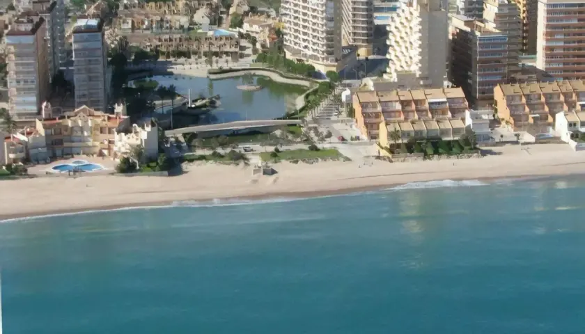 Vista aérea de la playa de la goleta, con edificios residenciales, una laguna artificial y el mar turquesa.