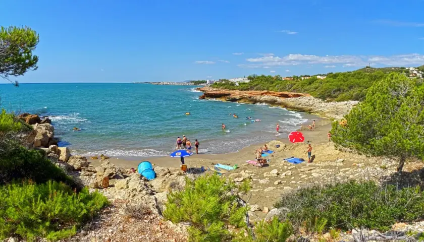Gente disfrutando del sol y el mar en la cala blanca de Castellón, con aguas turquesas y vegetación mediterránea.