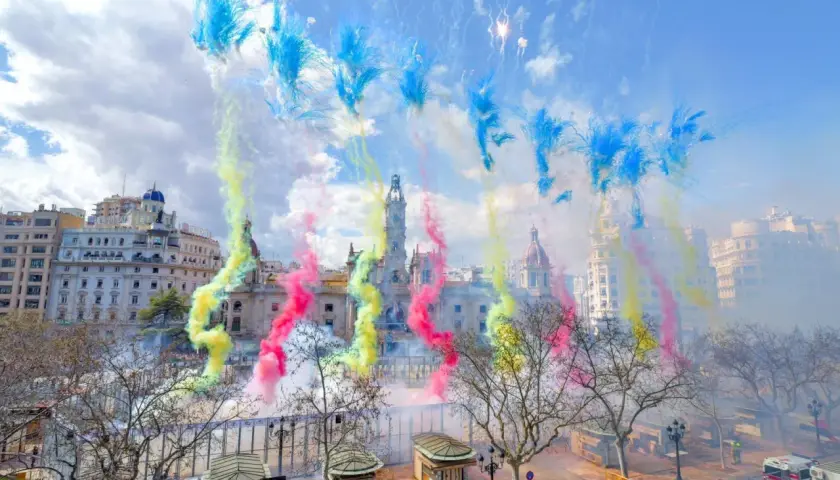Explosión de color y ruido en la mascletà hoy. El cielo se tiñe de azul, amarillo y rosa sobre edificios históricos.