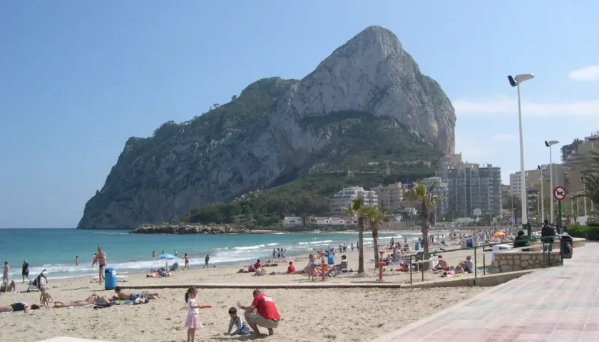 Gente disfrutando del sol y el mar en la playa de la Fossa, con el imponente peñón de Ifach de fondo.