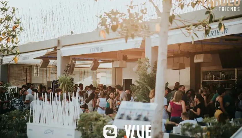 Gente disfrutando en Arribar, un lugar con ambiente de fiesta. El logo de @VLUE destaca.