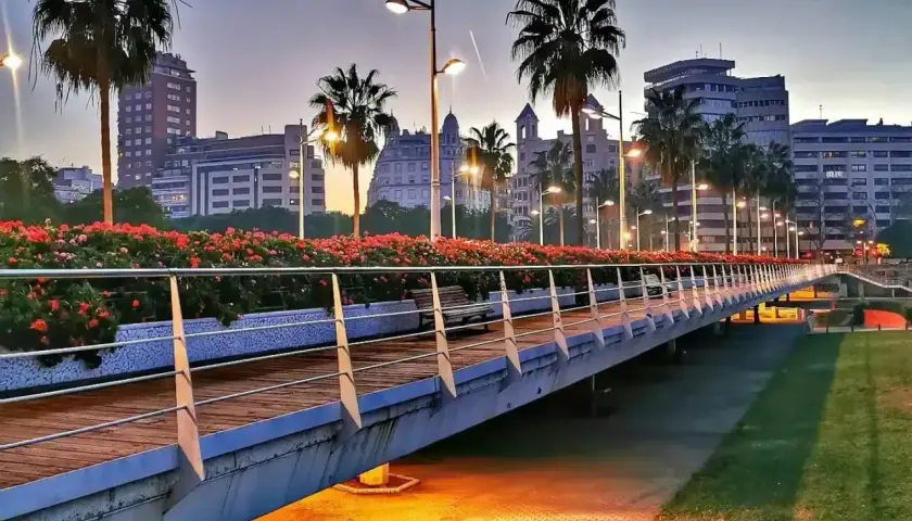 Puente iluminado con palmeras y flores rojas en la ciutat vella valencia al atardecer.