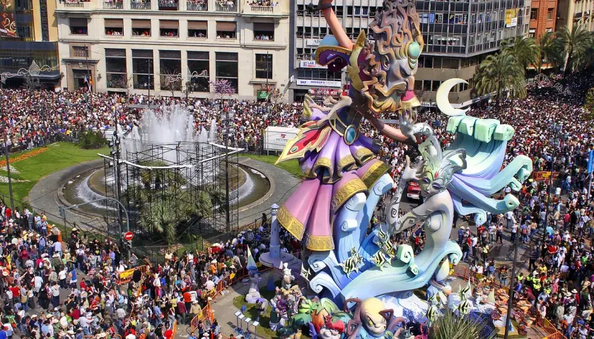 Gigantescas figuras de las mejores Fallas de Valencia, rodeadas de miles de personas, celebran la fiesta en una plaza con fuente.