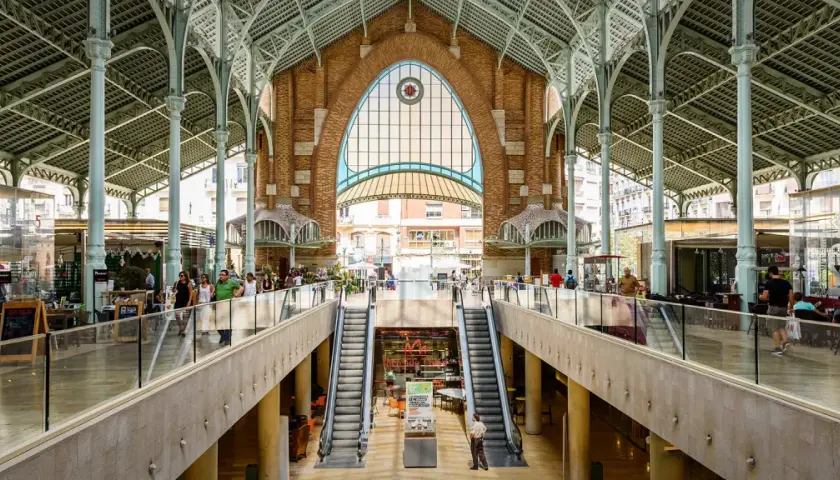 Interior del Mercado de Colón, con sus arcos de hierro y cristal, escaleras mecánicas y puestos de comida.