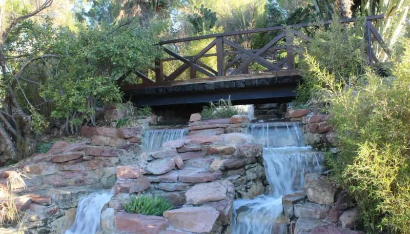 Puente de madera sobre cascadas en uno de los parques de Valencia. Naturaleza exuberante y rocas rojizas crean un paisaje idílico.