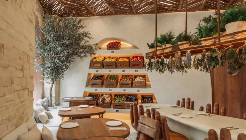 Interior de restaurantes en Valencia con encanto, con estanterías de frutas y verduras frescas, un olivo y mesas de madera.