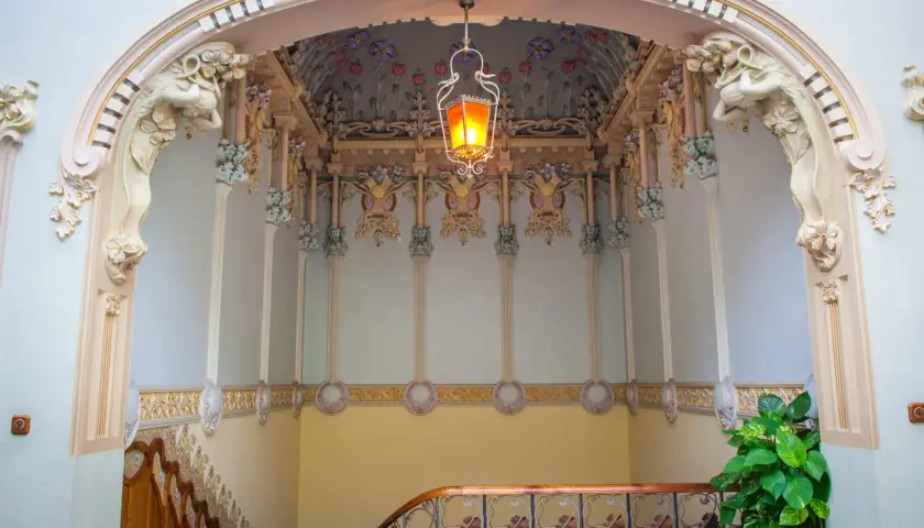 Detalles ornamentales de una casa modernista en Novelda, con una lámpara colgante y motivos florales en el techo.
