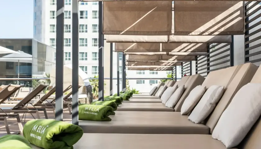 Tumbonas listas para el relax en la terraza del Meliá Valencia, con toallas verdes y vistas a la ciudad.