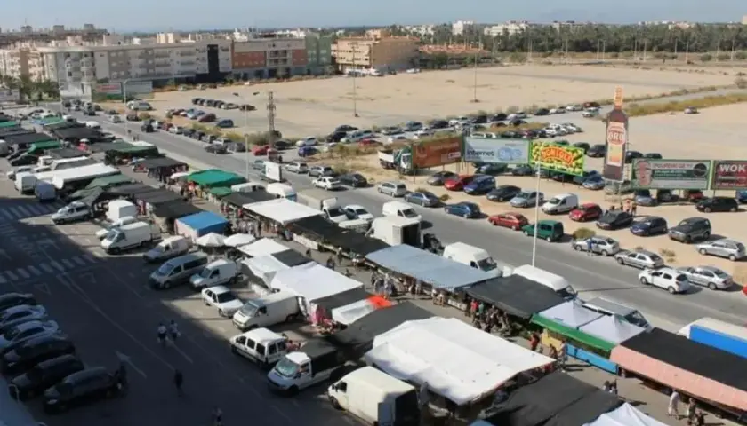 Vista aérea de un bullicioso mercadillo en Elche, con puestos, furgonetas y coches aparcados.
