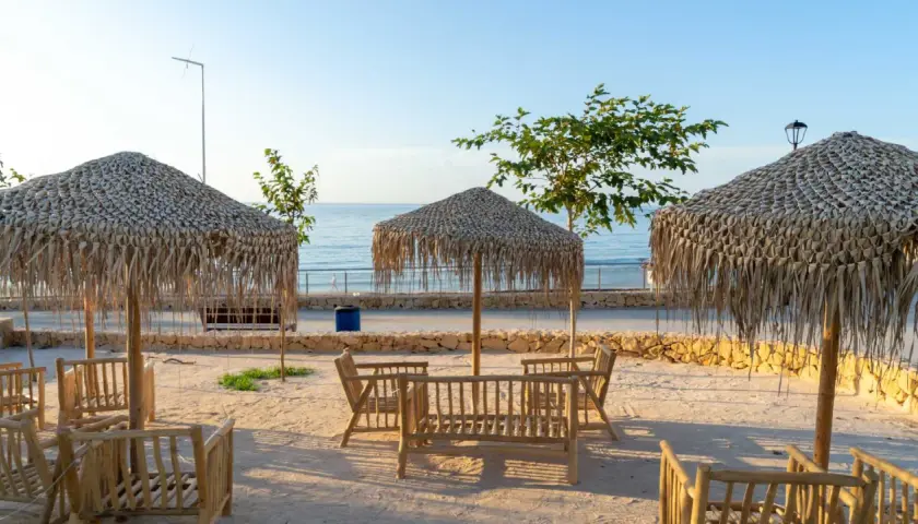 Mesas de madera y sombrillas de paja en la cala Lanuza, listas para disfrutar del mar y el sol.