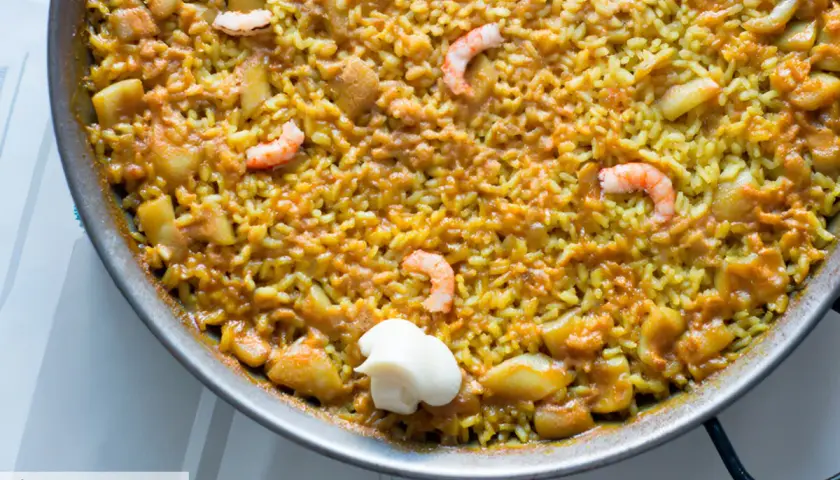 Un delicioso arroz a banda que lleva gambas y trozos de patata, servido en paellera con una cucharada de alioli.