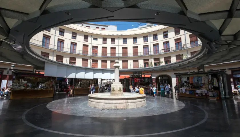 Fuente central en la plaza redonda valencia, rodeada de edificios curvos y puestos de venta.