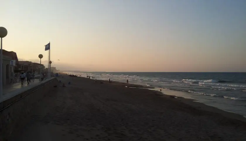 Gente pasea por la **playa de Piles** al atardecer, con el mar y el cielo en tonos pastel.