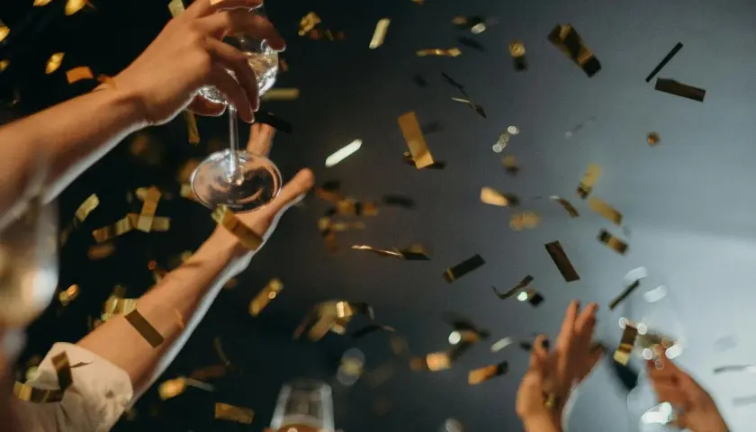 Manos brindando con copas y confeti dorado cayendo. ¡Una celebración perfecta para saber qué hacer en Nochevieja en Valencia!