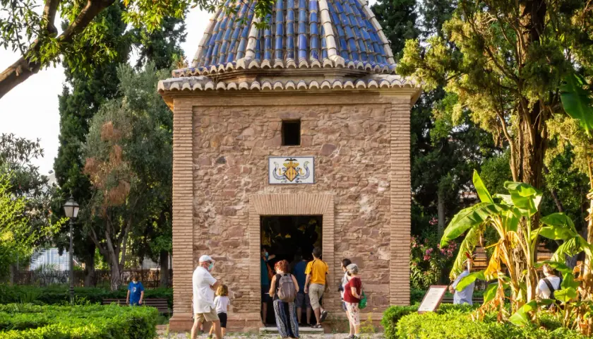 La ermita de Sant Jordi, con su cúpula azul y fachada de piedra, recibe a visitantes entre exuberante vegetación.