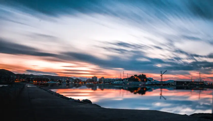 Atardecer en un puerto, con reflejos vibrantes en el agua. ¿Costa Blanca o Costa del Sol? La belleza es innegable.
