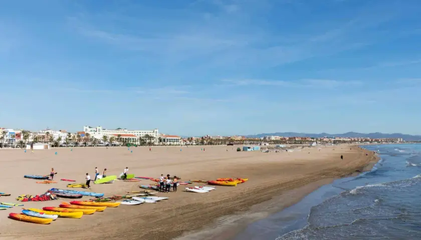 Gente prepara kayaks y tablas en la playa Malvarrosa, lista para un día de sol y mar.