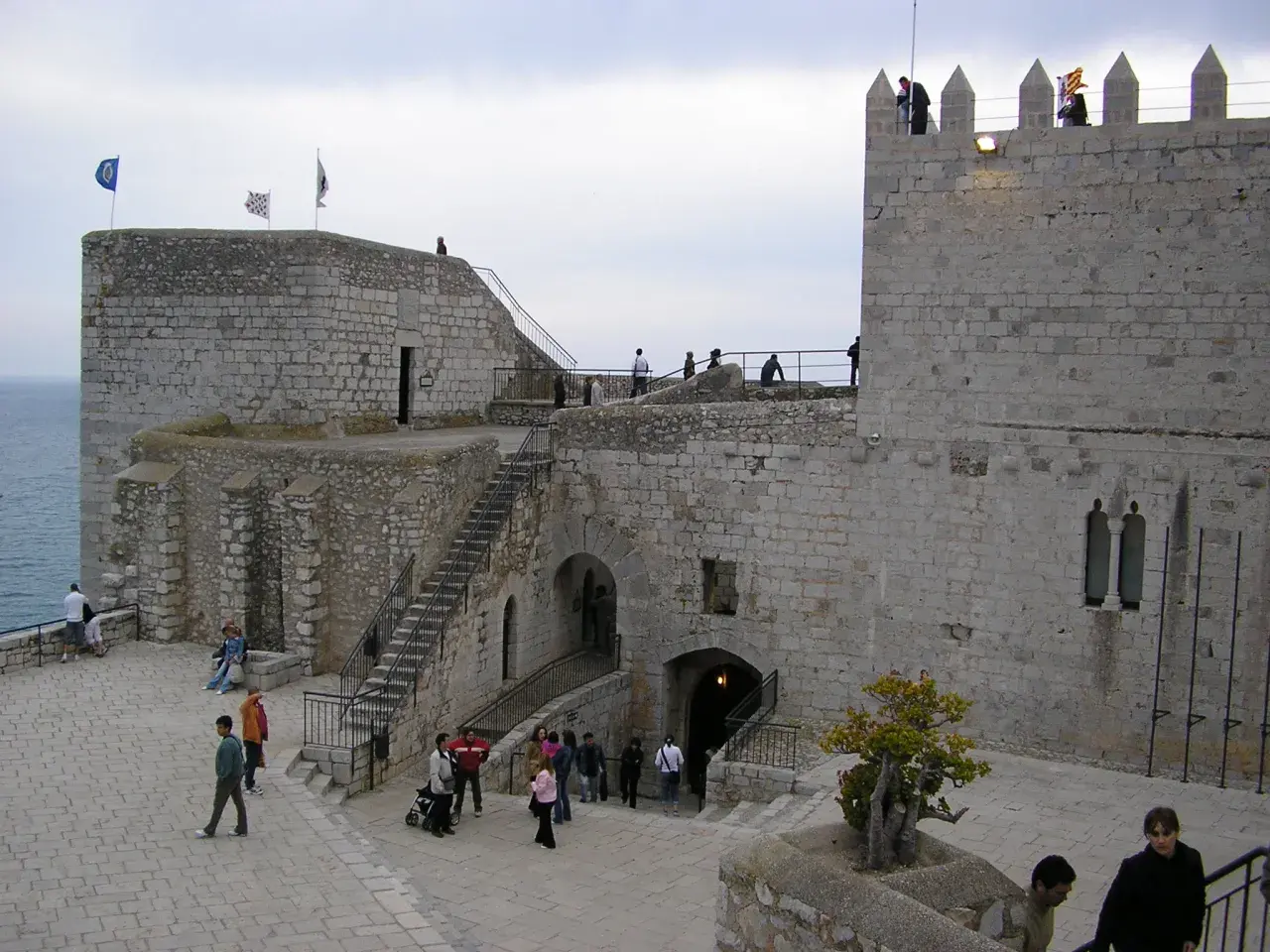 El castillo del Papa Luna en Peñíscola, con sus murallas de piedra y escalinatas, recibe a visitantes que pasean por sus patios.