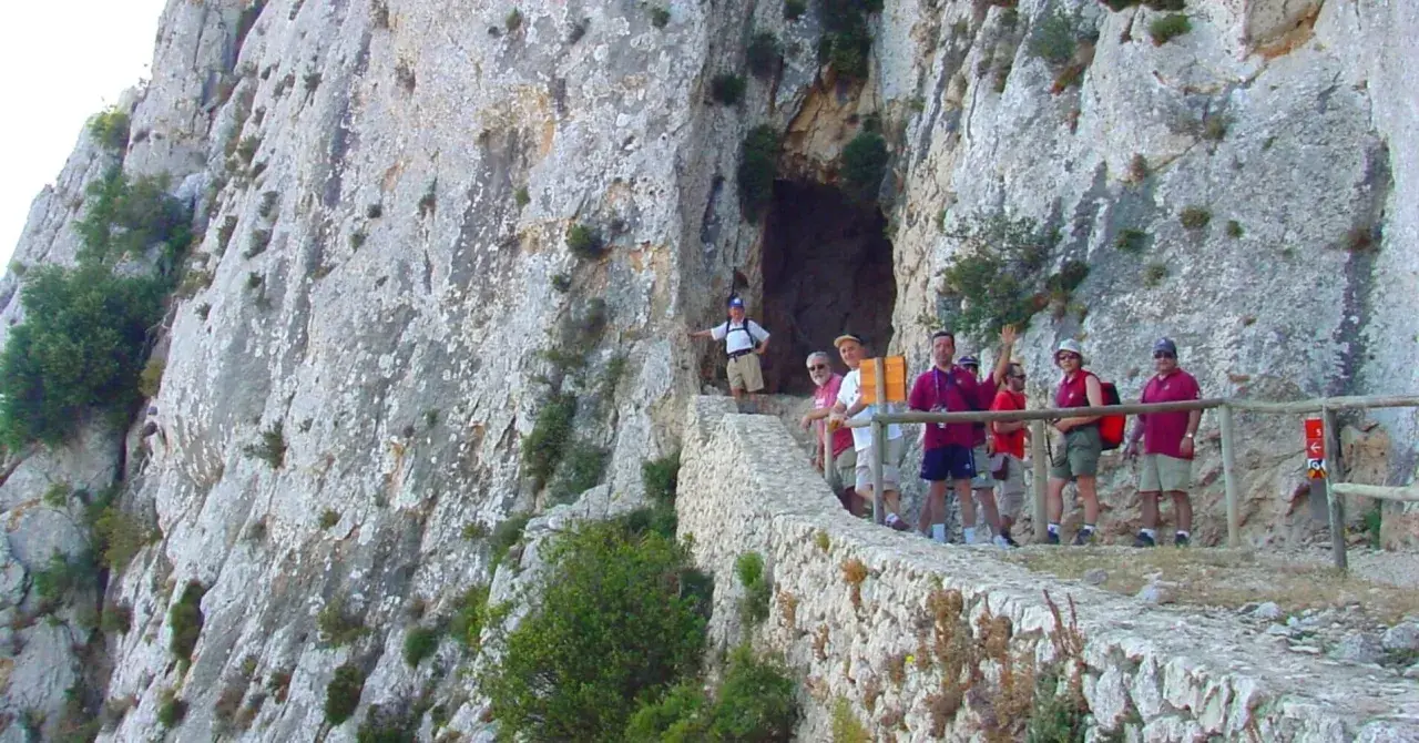 Grupo de excursionistas en el sendero del Peñón de Calpe, con una cueva a la izquierda y vistas rocosas.
