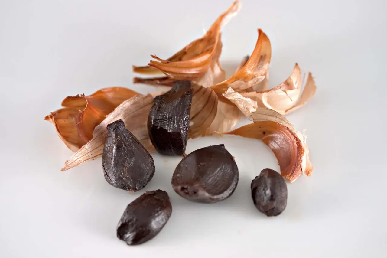 Dientes de ajo negro, con cáscaras secas de color naranja y blanco, evocan el sabor único del ajo negro alicante.
